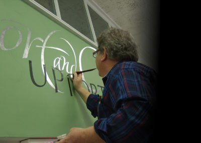 Calligraphy Lettering John Stevens brush-lettering a wall at Associated Artists