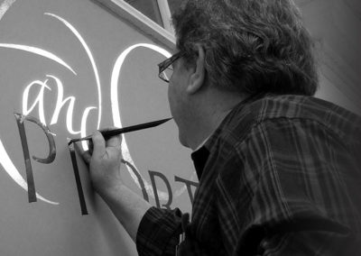 Calligraphy Lettering John Stevens brush-lettering a wall at Associated Artists